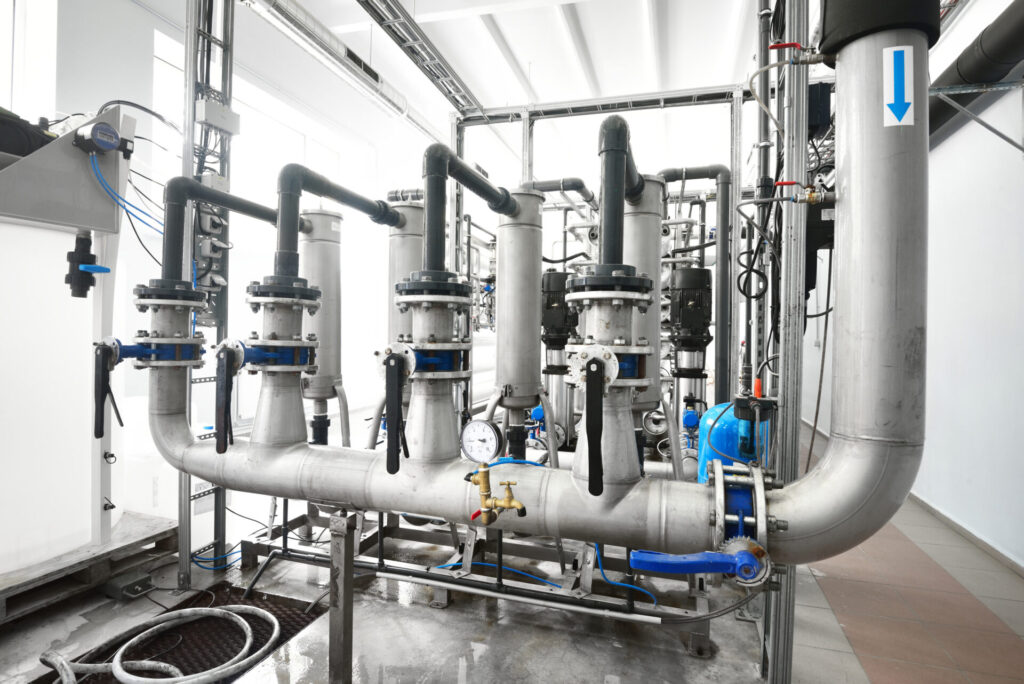 Large industrial water treatment and boiler room. Shiny steel metal pipes and blue pumps and valves.